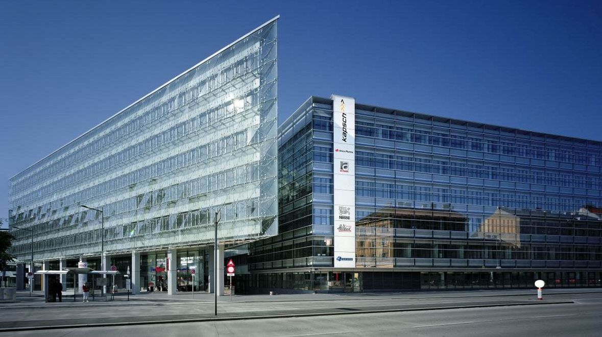 Photo: office building with a tapered glass façade; in front of it a multi-lane road